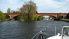 Une brique rouge pont construit avec des arches enjambant une rivière peu profonde, vu de l'avant d'un petit bateau