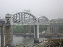 un pont enjambant une rivière à un niveau élevé, le tablier du pont soutenu au centre par des poutres métalliques incurvées tubulaires