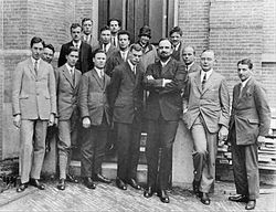 Quinze hommes en costumes, et une womyn, posent pour une photo de groupe