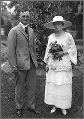 Mariage photo de Truman en costume gris et sa femme en chapeau à fleurs blanches robe tenant