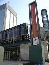 Le Centre de musique Francis Winspear avec une bannière en face de la tour Edmonton Symphony Orchestra et Century Place derrière elle.