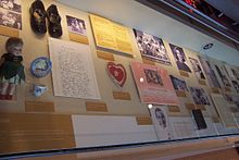 Musée vitrine contenant des photographies, des documents, des chaussures, poupée, et d'autres objets de la petite enfance