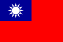 Un drapeau rouge, avec un petit rectangle bleu dans le coin supérieur gauche sur lequel se trouve un soleil blanc composé d'un cercle entouré par 12 rayons.