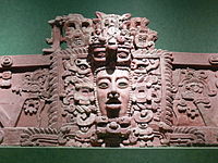 Section de frise en stuc avec un visage humain de premier plan dans le centre, entouré de décoration élaborée.