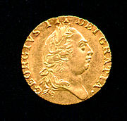 Moeda de ouro que carrega o perfil de um homem de cabeça redonda vestindo um corte de cabelo em estilo clássico romano e louro-coroa de flores.
