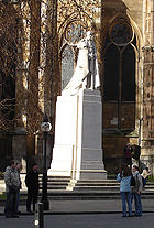Branco estátua de pedra de George V em vestes de liga sobre um pedestal da mesma pedra que está em uma rua