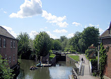 Canal fluindo longe do fotógrafo divide-se em dois canais com um lado direito chegar no comportas. Para o é um edifício e para a direita de uma trilha e um pub.