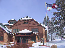 Dois andares edifício de madeira ao lado de pólo de bandeira com a bandeira dos Estados Unidos que acena no vento. Neve no chão.
