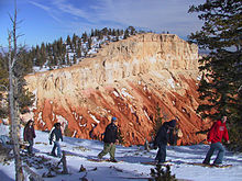 Uma linha de snowshoers com penhasco rocha colorida no fundo.