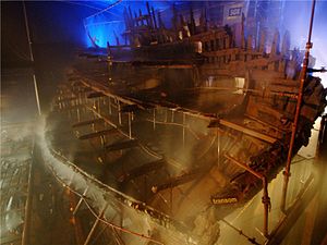 Uma secção diagonal de um navio de madeira visto a partir da popa dentro de um edifício moodily iluminadas enquanto está sendo pulverizada com água a partir de um sistema de aspersão