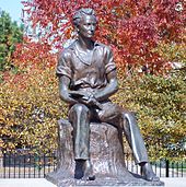 Uma estátua de Lincoln jovem sentado em um toco, segurando um livro aberto em seu colo
