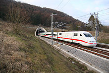 Branco trem elétrico com cheatline vermelho que emerge do túnel na zona rural