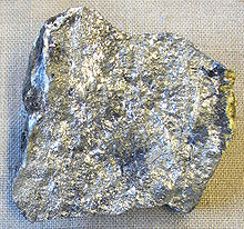 Um pedaço irregular de pedra prateado com manchas de variação de brilho e sombra.