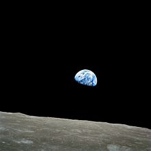 The small blue-white semicircle of the Earth, almost glowing with colour in the blackness of space, rising over the limb of the desolate, cratered surface of the Moon.