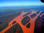 Fotografia aérea de um rio bifurcado que ficou vermelho devido ao escoamento superficial do solo vermelho.