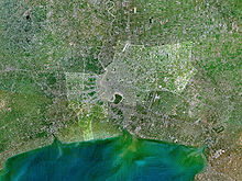 Imagem de satélite mostrando um rio que flui para o mar, com grandes áreas construídas ao longo de seus lados, pouco antes da foz do rio