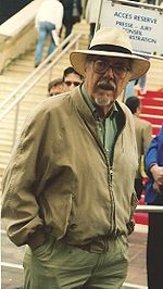 Photo of the director Robert Altman in his mid-60s, wearing a goatee, glasses, a wide-brimmed white hat and a jacket and looking directly into the camera.