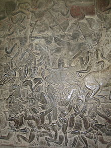 Um relevo de pedra preto que descreve um número de homens vestindo uma coroa e um dhoti, lutando com lanças, espadas e arcos. Um carro com metade do cavalo para fora da moldura é visto no meio.