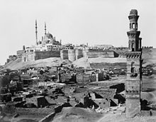 Uma mesquita multi-cúpula domina o Citadel murada, com túmulos em ruínas e um minarete solitário na frente.