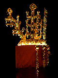 Uma coroa de ouro brilhante que se assemelha árvores, exibido em um quarto muito escuro. Tem grânulos de cristal de rocha e translúcidas e curvas ornamentos de jade verde