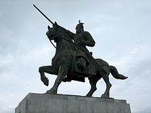 Uma estátua de bronze de um cavaleiro de armadura em um cavalo de equitação contra céus sombrios