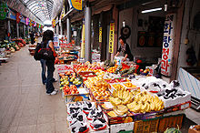 Um cliente do sexo feminino visitando uma loja de fruta. Banana and grapes are displayed on the front.