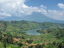 Fotografia de um lago com uma das montanhas Virunga atrás, parcialmente em nuvem