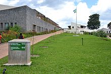 Photograph depicting a hospital building, with Rwandan flag, viewed from the entrance pathway