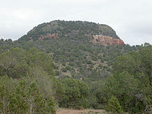 Um grande monte de rocha e da sujeira com avermelhada e acinzentada do solo e principalmente coberto com vegetação.