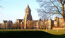 Um tiro largo de uma escola de Inglês velho com uma torre central, um campo desportivo é visto em primeiro plano.