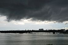 Escuras nuvens de tempestade sobre um corpo d'água com edifícios no fundo distante