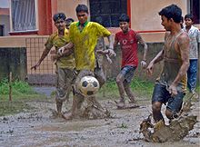 several young men playing association football in a muddy field in the rain