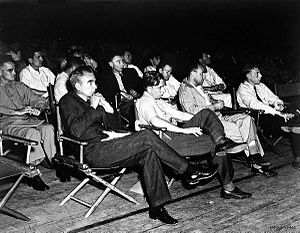 Um grupo de homens em mangas de camisa sentadas em cadeiras dobráveis.