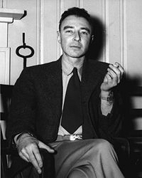A man in a suit seated, smoking a cigarette.