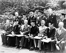 A group of men in uniforms, suits and academic dress sit for a formal group photograph