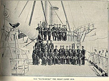 Arma naval grande a bordo de um navio de guerra, com officier sentado no deck abaixo e acima da arma.