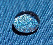 A shiny spherical drop of water on blue cloth.