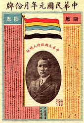 A calendar with a picture of a Chinese man in the center. On top of it stands a flag with five horizontal stripes (red, yellow, blue, white and black).