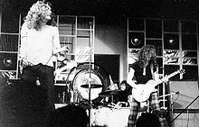 Uma fotografia preto e branco de Robert Plant tocando com suporte do microfone e Jimmy Page com guitarra