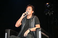 Um homem sentado em uma cadeira e falar em um microfone