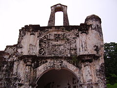 Stained ruína de um edifício de pedra, mostrando um arco central, ladeado por duas colunas, com um relevo de pedra acima do arco, também ladeado por duas colunas, e um segundo arco free-standing empoleirada no topo da ruína.