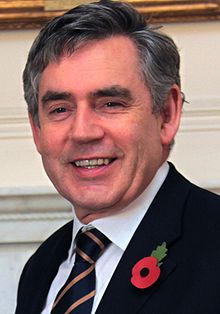 Cabeça e ombros de um homem sorridente em um terno e gravata listrada com escuro, cabelos grisalhos e rosto arredondado com queixo quadrado