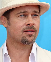 A caucasiano com o cabelo castanho claro, olhos azuis e barba curta marrom, na frente de um fundo de turquesa. Ele está vestindo uma camisa branca e chapéu branco.
